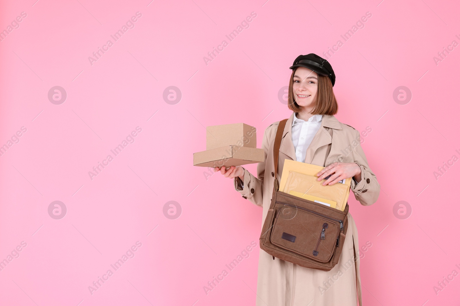 Photo of Happy postwoman with bag and parcels on pink background. Space for text