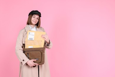 Photo of Happy postwoman with bag and envelopes on pink background. Space for text