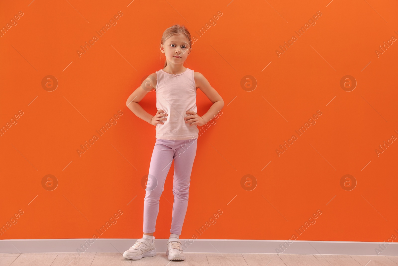 Photo of Little girl in sportswear near orange wall indoors, space for text