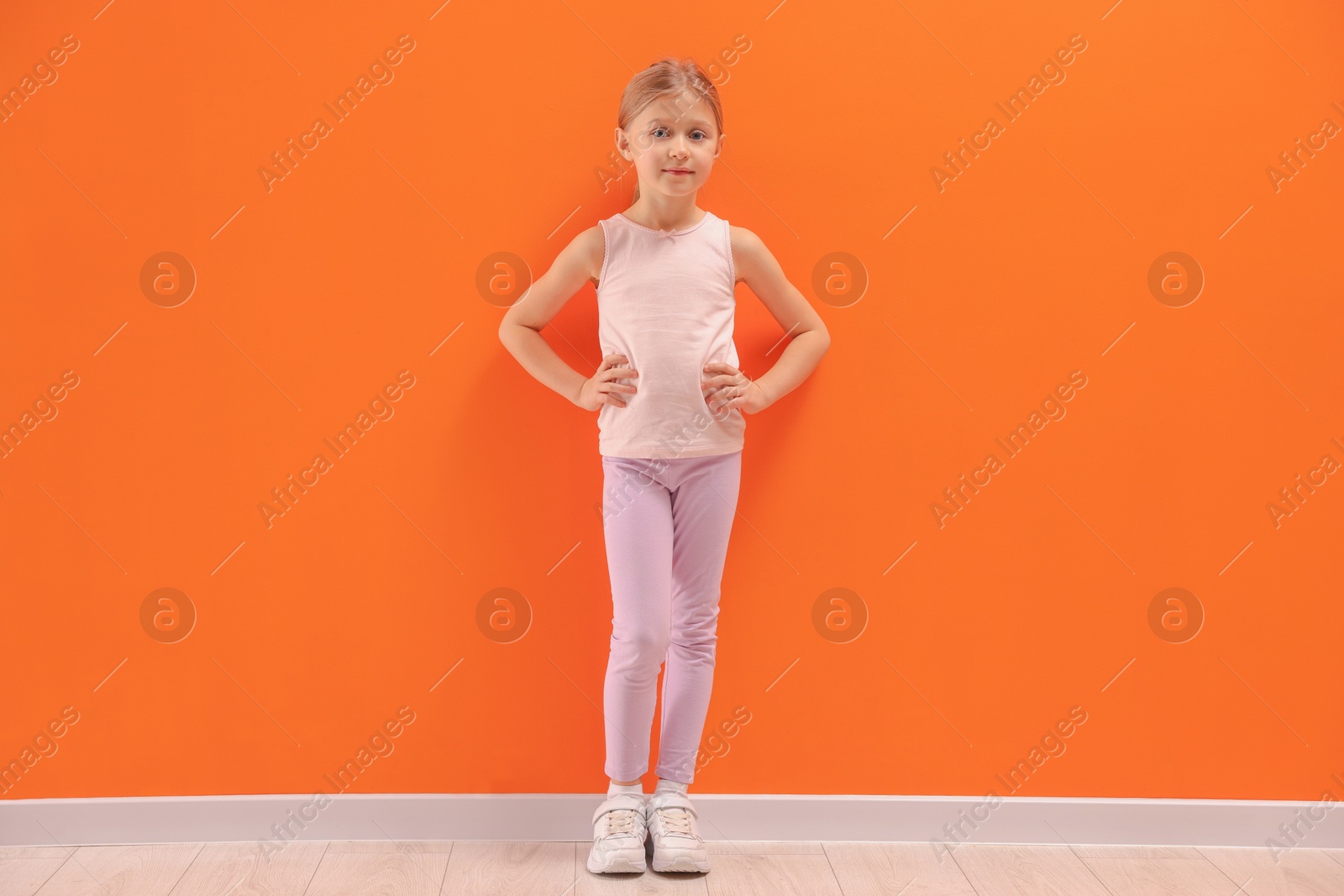 Photo of Little girl in sportswear near orange wall indoors