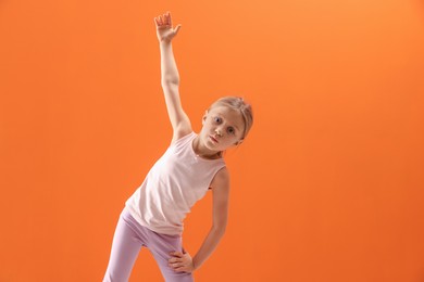 Photo of Cute little girl exercising on orange background, space for text