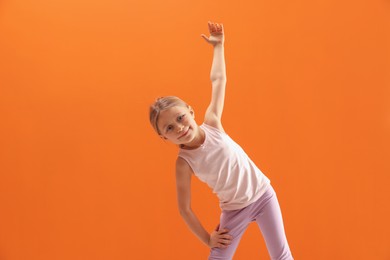 Photo of Cute little girl exercising on orange background, space for text