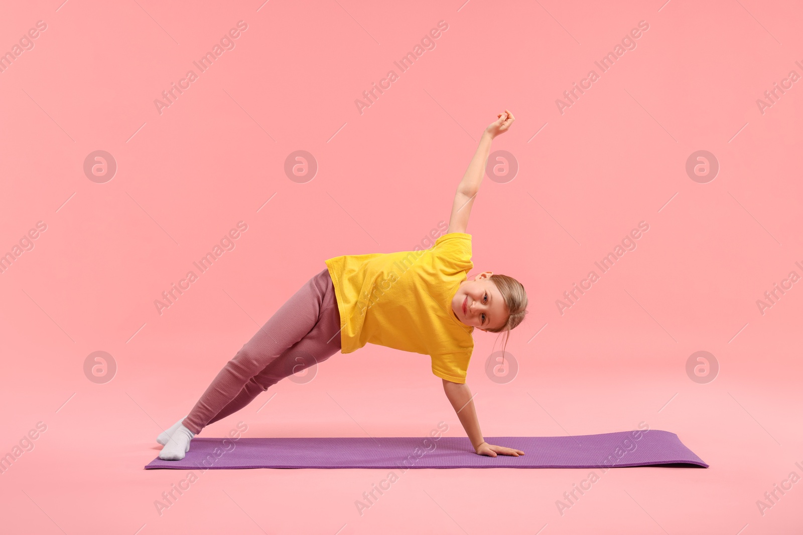 Photo of Cute little girl exercising on fitness mat against pink background