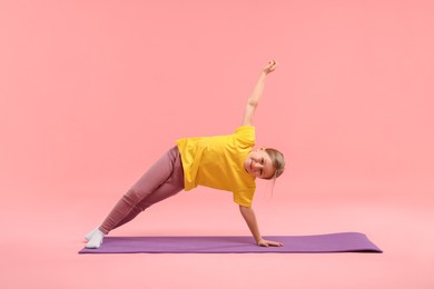 Photo of Cute little girl exercising on fitness mat against pink background