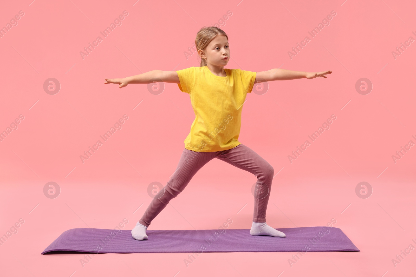 Photo of Cute little girl exercising on fitness mat against pink background