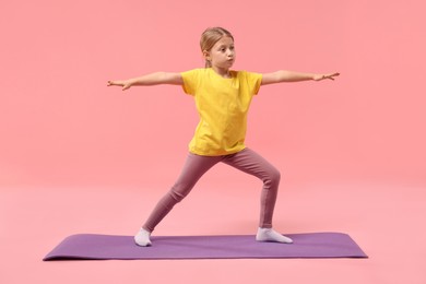 Photo of Cute little girl exercising on fitness mat against pink background