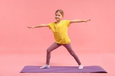 Photo of Cute little girl exercising on fitness mat against pink background