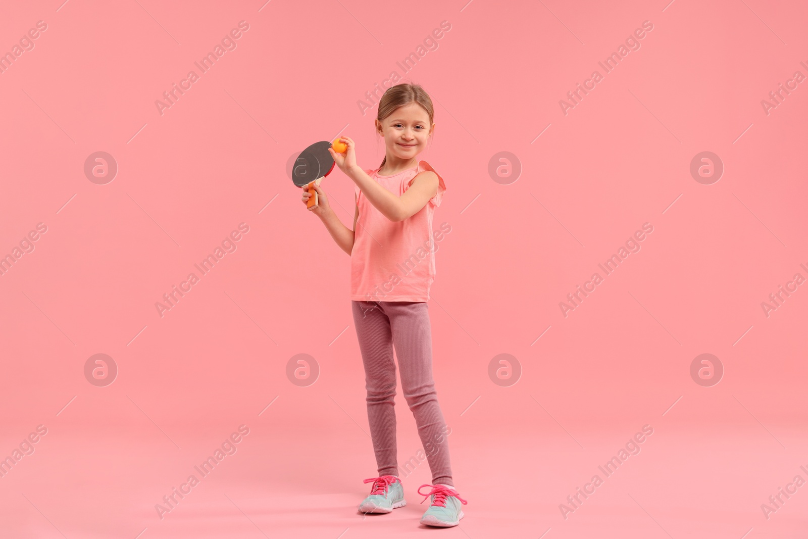 Photo of Cute little girl with ping pong racket and ball on pink background