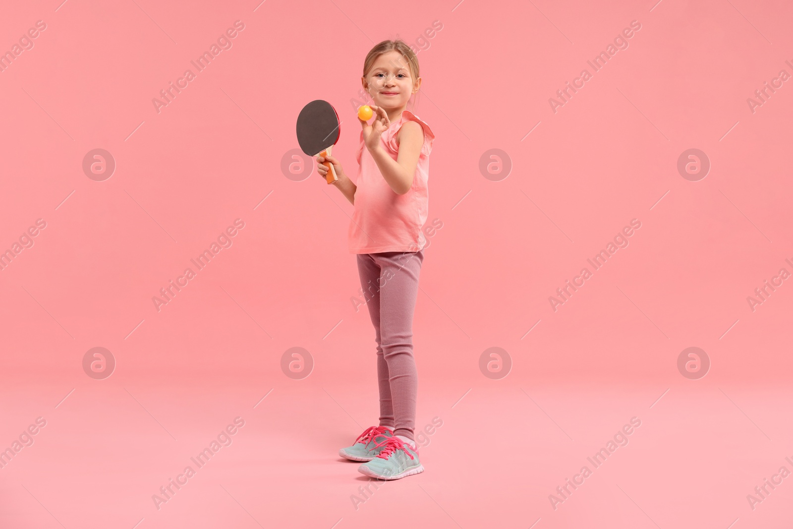 Photo of Cute little girl with ping pong racket and ball on pink background