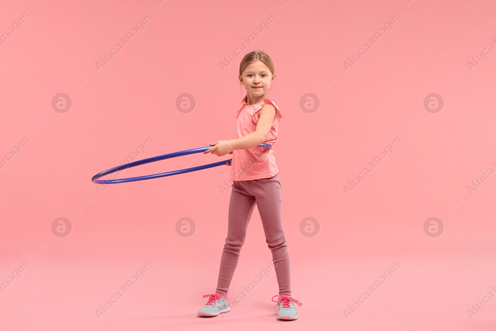 Photo of Cute little girl exercising with hula hoop on pink background