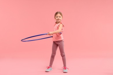 Photo of Cute little girl exercising with hula hoop on pink background