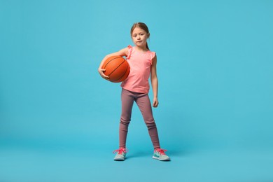 Photo of Cute little girl with basketball ball on light blue background