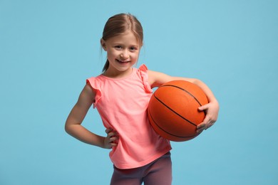 Photo of Cute little girl with basketball ball on light blue background