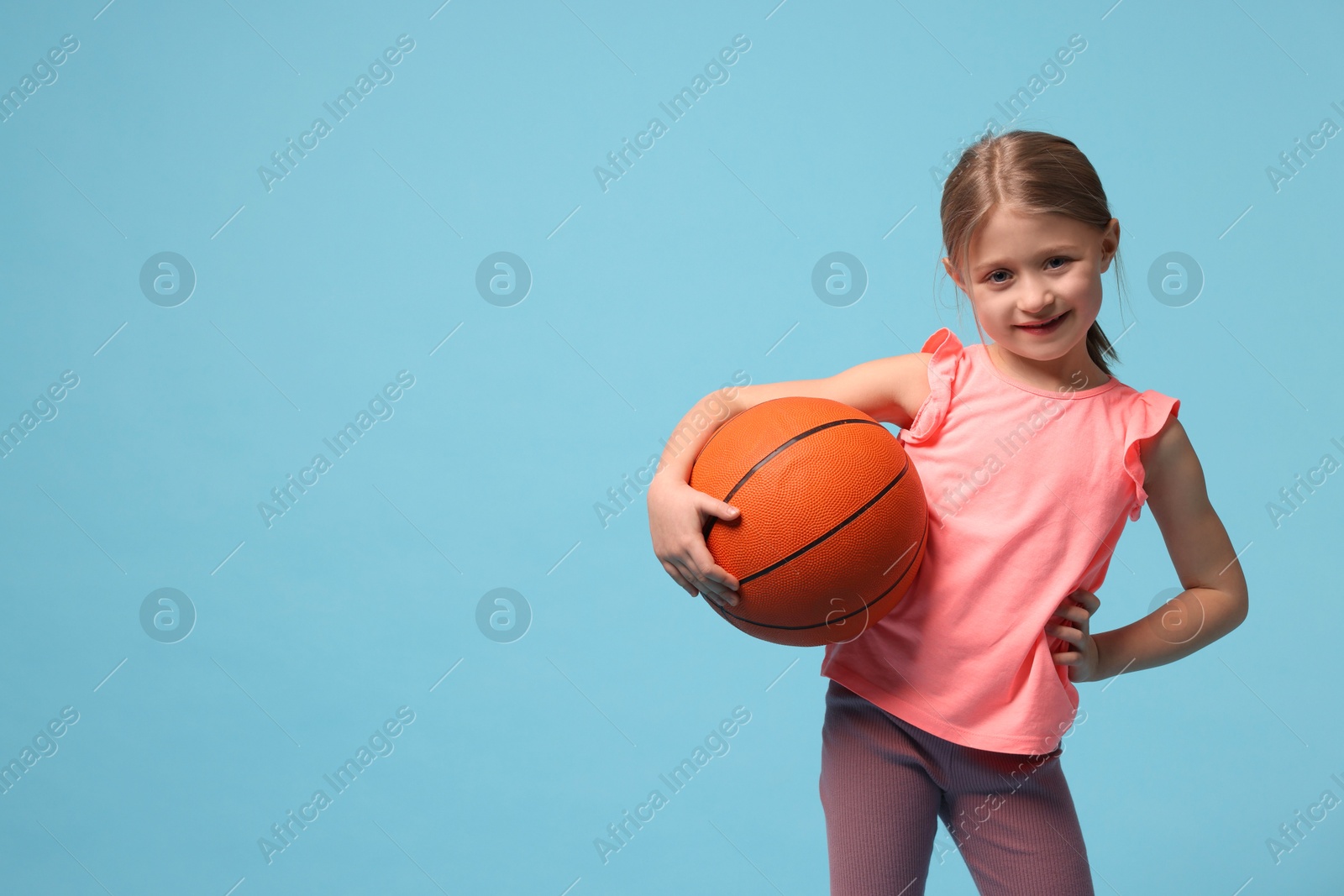 Photo of Cute little girl with basketball ball on light blue background, space for text