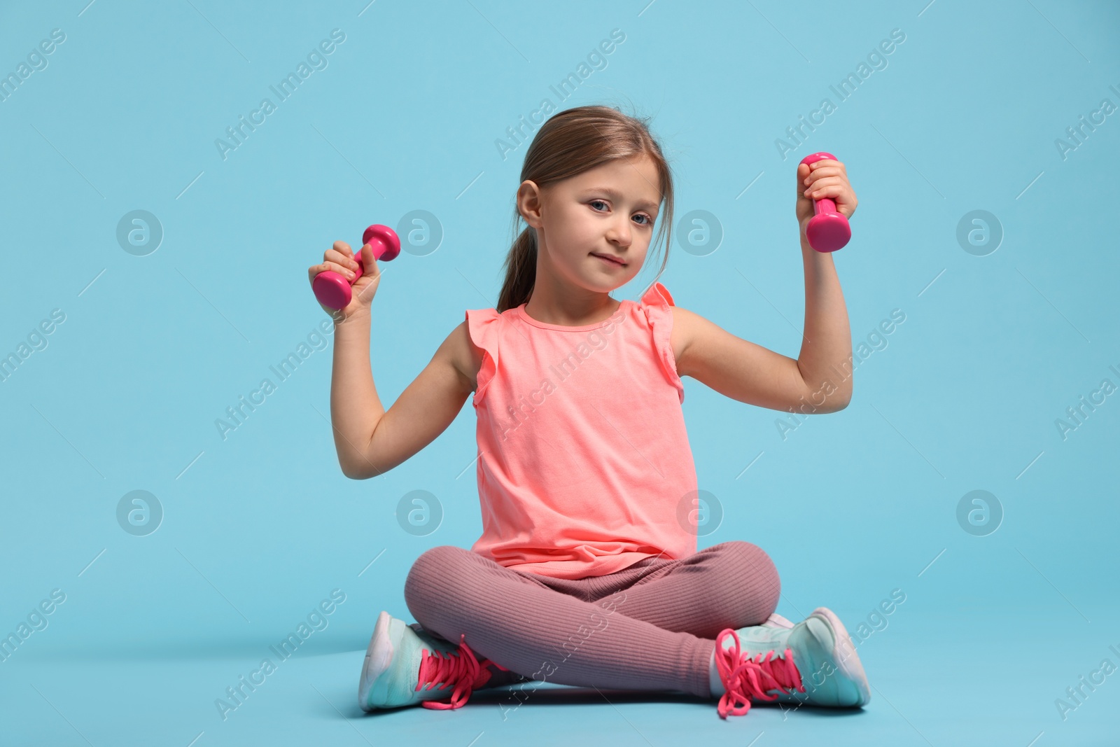 Photo of Cute little girl exercising with dumbbells on light blue background