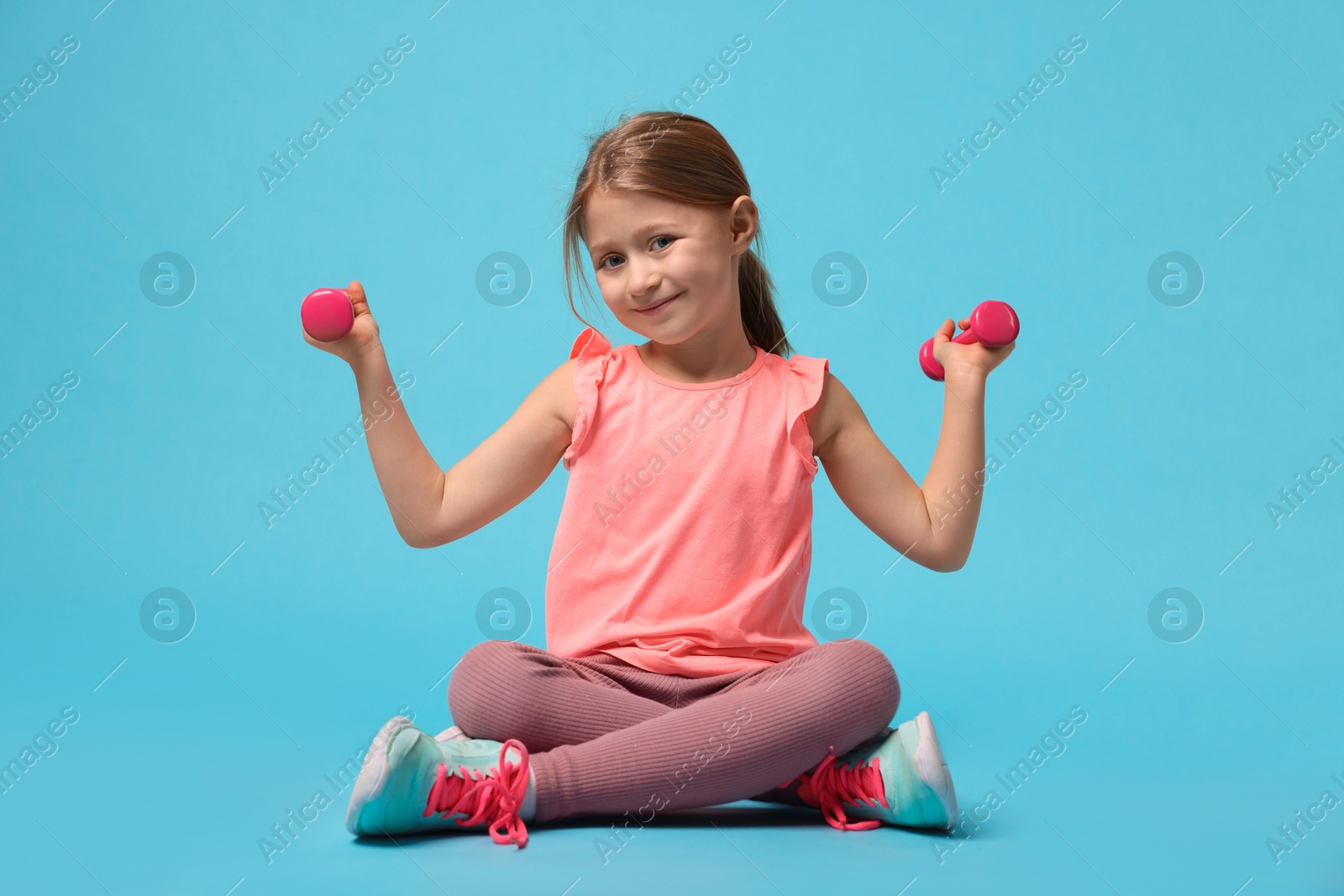 Photo of Cute little girl exercising with dumbbells on light blue background