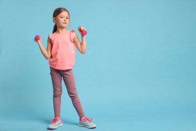 Photo of Cute little girl exercising with dumbbells on light blue background, space for text