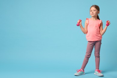 Photo of Cute little girl exercising with dumbbells on light blue background, space for text