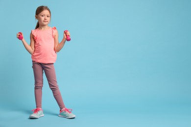 Photo of Cute little girl exercising with dumbbells on light blue background, space for text