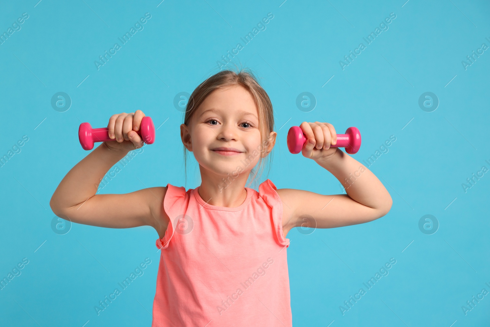 Photo of Cute little girl exercising with dumbbells on light blue background