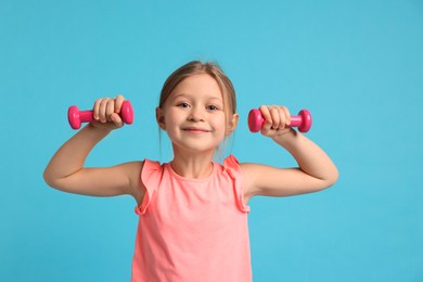 Photo of Cute little girl exercising with dumbbells on light blue background