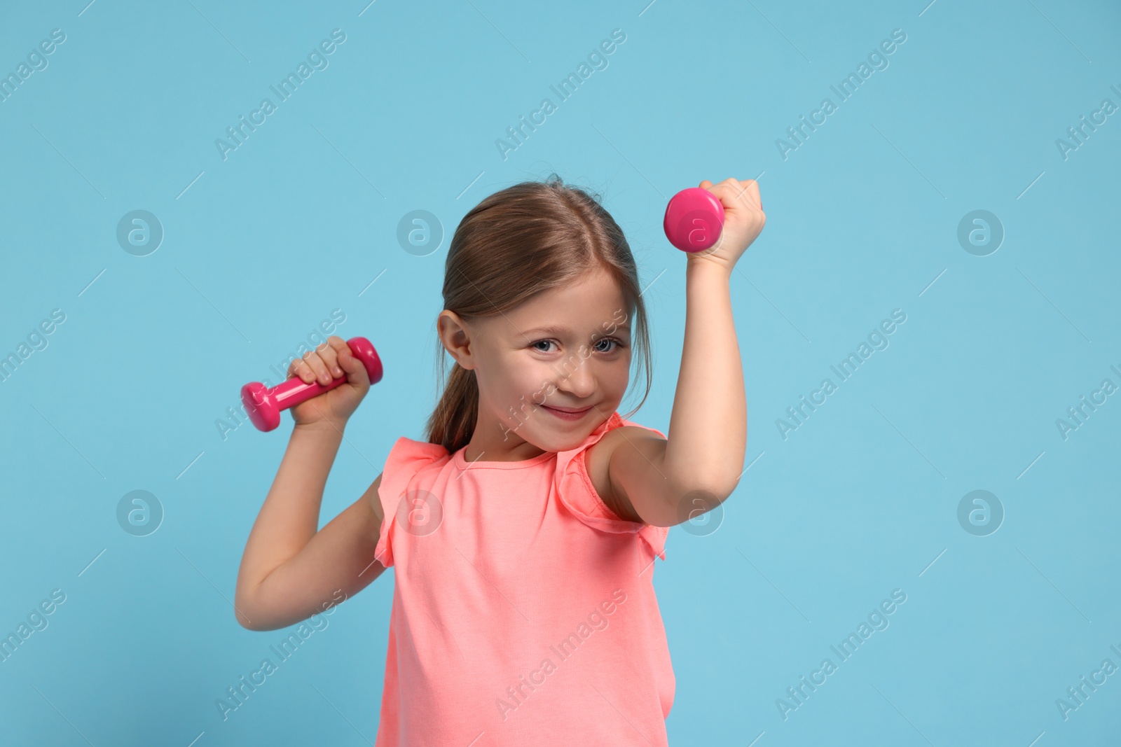 Photo of Cute little girl exercising with dumbbells on light blue background