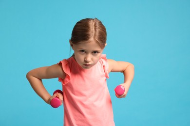 Photo of Cute little girl exercising with dumbbells on light blue background