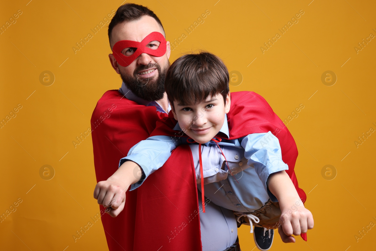 Photo of Father and his son wearing superhero costumes on orange background