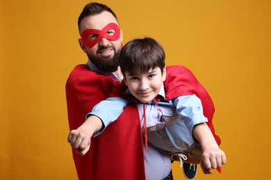 Photo of Father and his son wearing superhero costumes on orange background