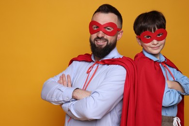 Photo of Father and his son wearing superhero costumes on orange background, space for text