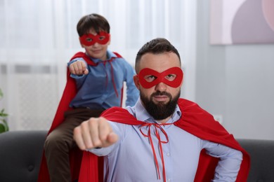 Photo of Father and his son wearing superhero costumes at home, selective focus