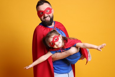 Photo of Father and his cute little daughter wearing superhero costumes on orange background