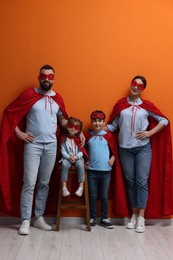 Photo of Parents and their children wearing superhero costumes near orange wall indoors