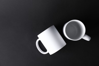 Photo of Two blank white mugs on black background, top view. Mockup for design