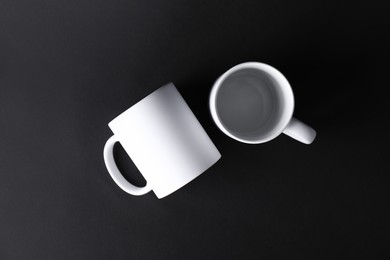 Photo of Two blank white mugs on black background, top view. Mockup for design