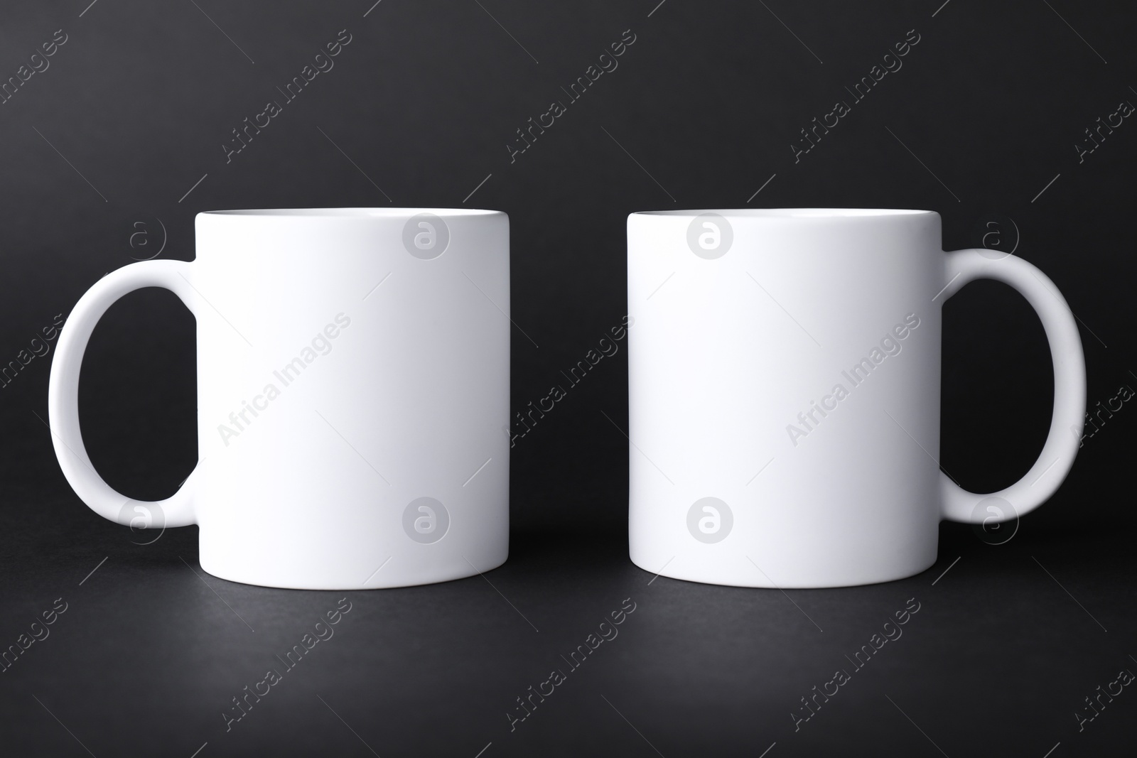 Photo of Two blank white mugs on black background. Mockup for design