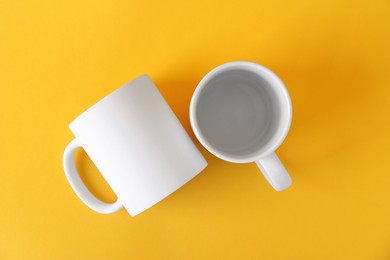 Photo of Two blank white mugs on yellow background, top view. Mockup for design