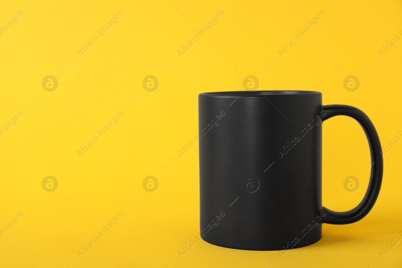 Photo of One blank black mug on yellow background. Mockup for design