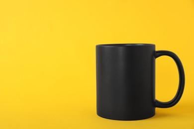 Photo of One blank black mug on yellow background. Mockup for design