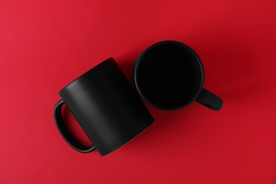 Photo of Two blank black mugs on red background, top view. Mockup for design