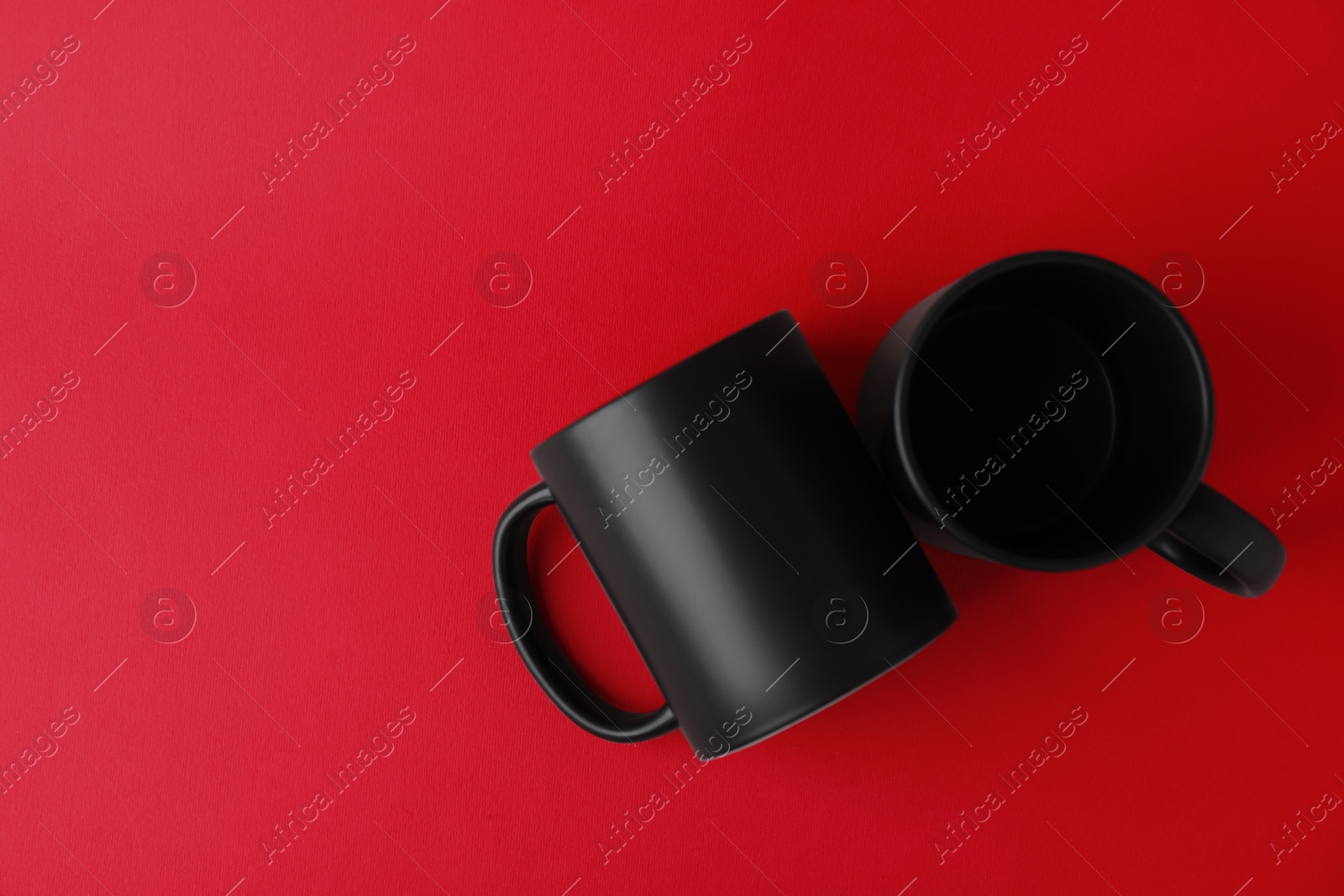 Photo of Two blank black mugs on red background, top view. Mockup for design