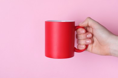 Photo of Woman holding blank red mug on pink background, closeup. Mockup for design