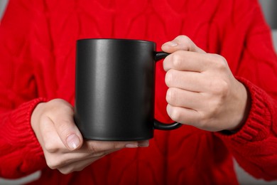 Photo of Woman holding blank black ceramic mug, closeup. Mockup for design