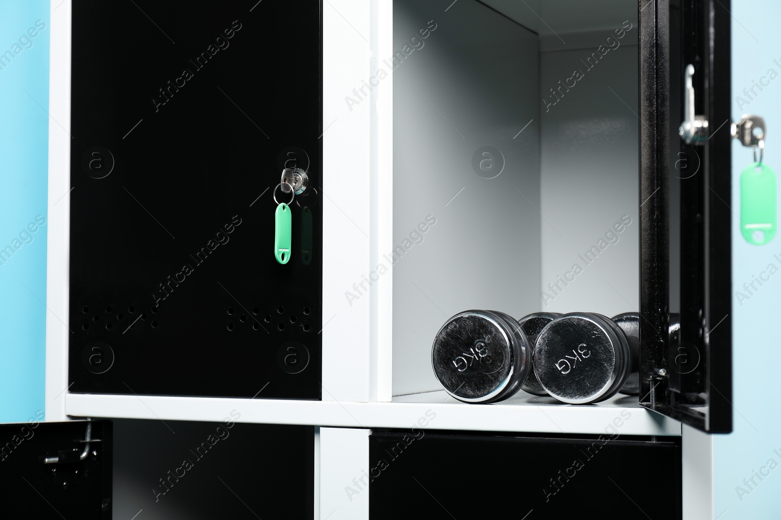 Photo of Open locker with dumbbells on light blue background, closeup