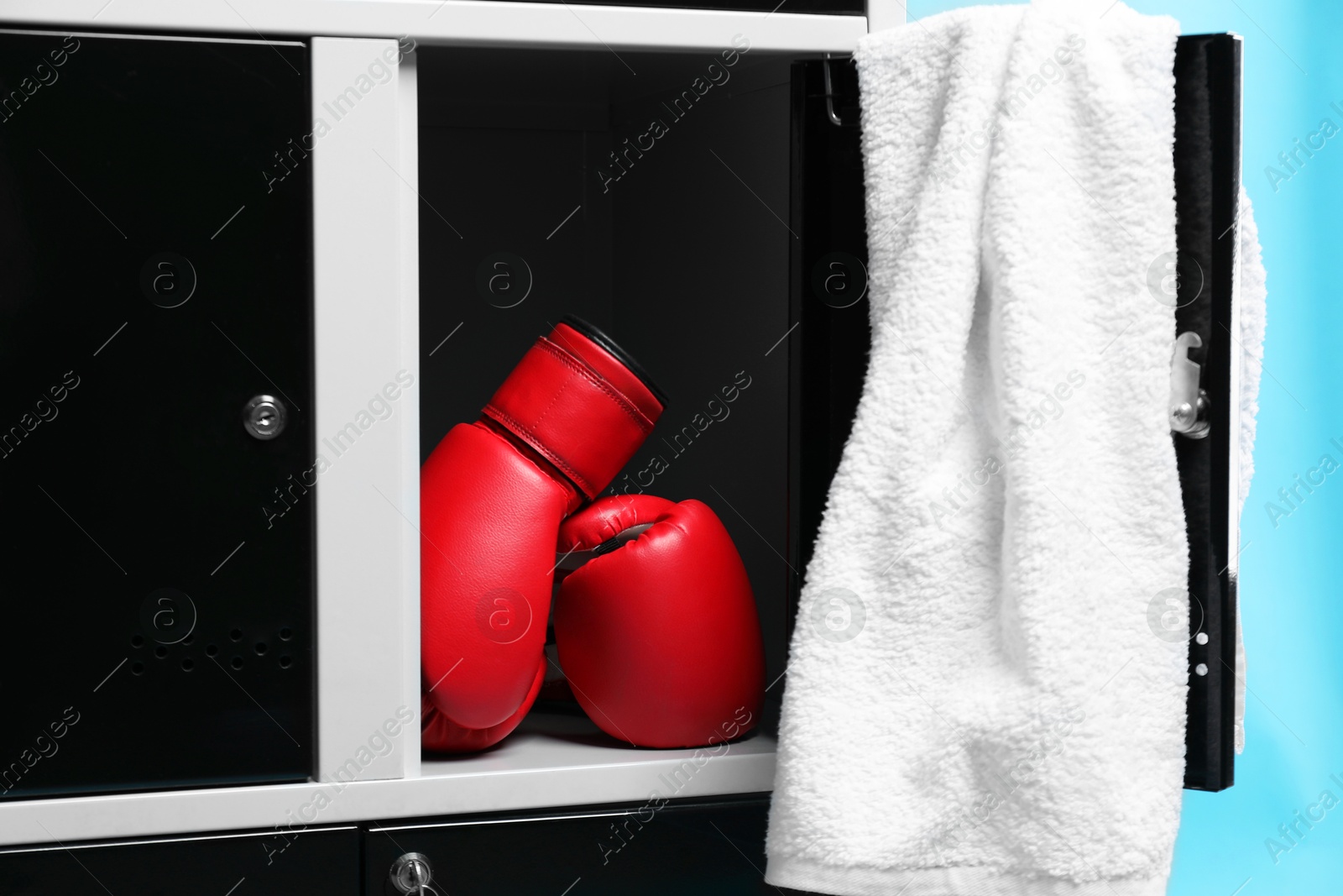 Photo of Open locker with boxing gloves and towel on light blue background, closeup