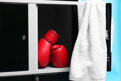 Open locker with boxing gloves and towel on light blue background, closeup