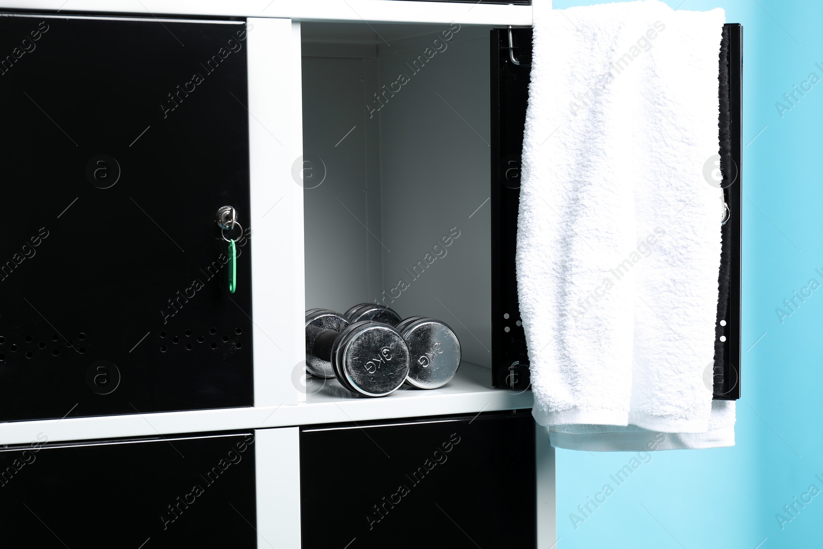 Photo of Open locker with dumbbells and towel on light blue background