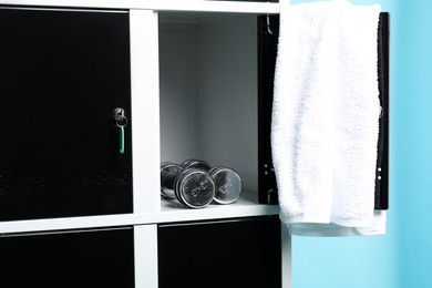 Open locker with dumbbells and towel on light blue background