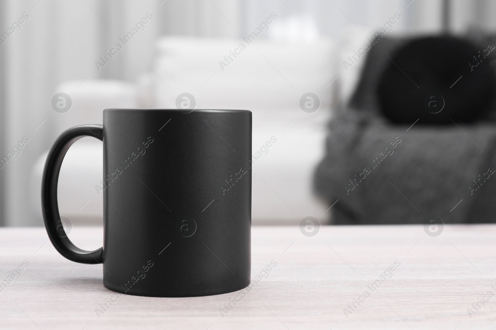 Photo of One blank black ceramic mug on white wooden table. Mockup for design