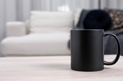 Photo of One blank black ceramic mug on white wooden table. Mockup for design